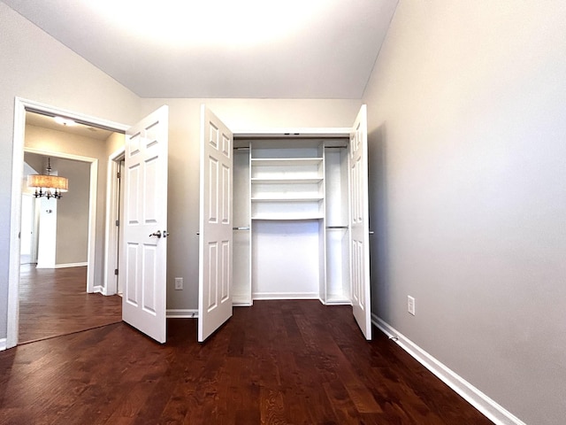 unfurnished bedroom featuring dark wood-style floors, a closet, a notable chandelier, and baseboards