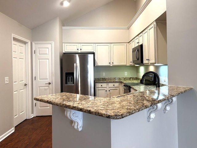 kitchen with lofted ceiling, dark stone countertops, stainless steel appliances, and a peninsula