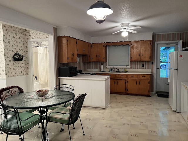 kitchen featuring brown cabinets, wallpapered walls, freestanding refrigerator, and light countertops