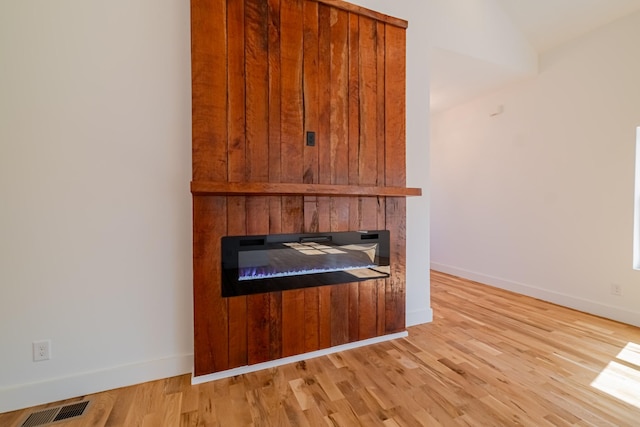 interior details featuring visible vents, baseboards, wood finished floors, and a glass covered fireplace