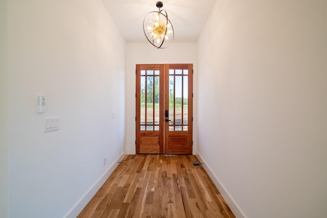 doorway featuring light wood-style floors, french doors, a chandelier, and baseboards