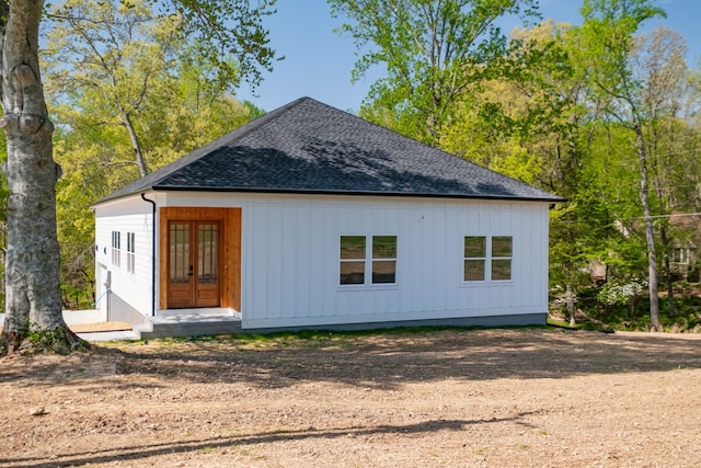 back of property with french doors, dirt driveway, and roof with shingles