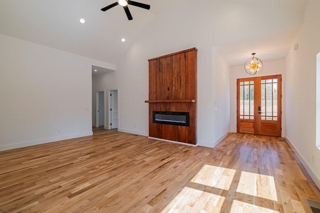unfurnished living room with light wood-style flooring, a large fireplace, french doors, high vaulted ceiling, and ceiling fan with notable chandelier