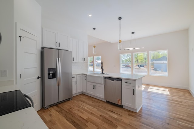 kitchen featuring light wood-style flooring, stainless steel appliances, white cabinets, a sink, and a peninsula