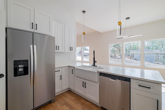 kitchen featuring a sink, light wood-style flooring, a peninsula, light countertops, and appliances with stainless steel finishes