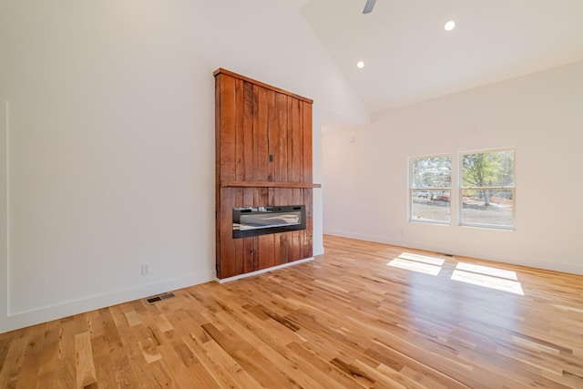 unfurnished living room with a fireplace, high vaulted ceiling, light wood-style flooring, and baseboards