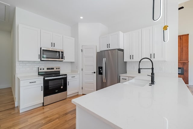 kitchen featuring white cabinetry, decorative backsplash, a sink, stainless steel appliances, and light wood finished floors
