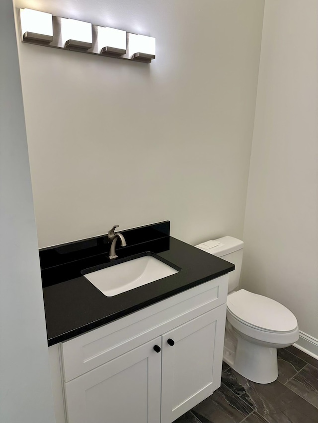 bathroom featuring toilet, baseboards, and vanity