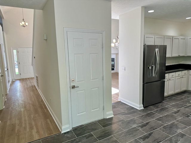 kitchen featuring white cabinets, dark countertops, stainless steel fridge, a chandelier, and baseboards