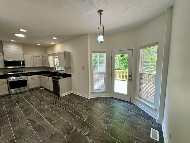 kitchen with dark countertops, a sink, stainless steel appliances, baseboards, and visible vents