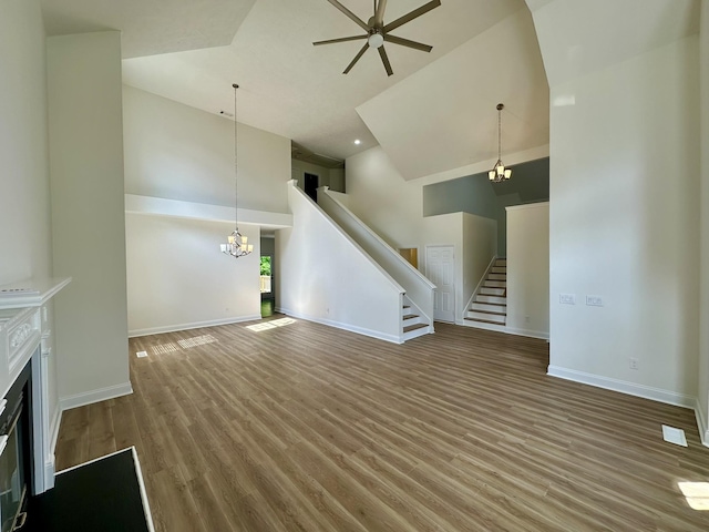 unfurnished living room featuring high vaulted ceiling, ceiling fan with notable chandelier, stairs, baseboards, and wood finished floors