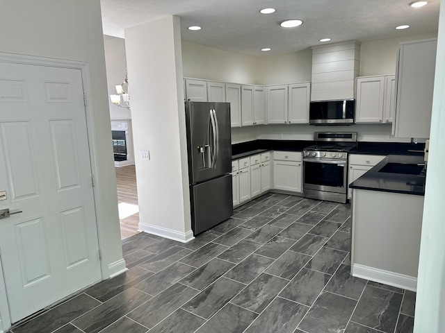 kitchen with dark countertops, appliances with stainless steel finishes, a sink, white cabinetry, and baseboards