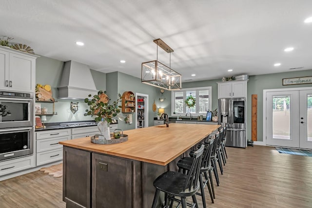 kitchen featuring light wood finished floors, recessed lighting, stainless steel appliances, wall chimney range hood, and butcher block counters