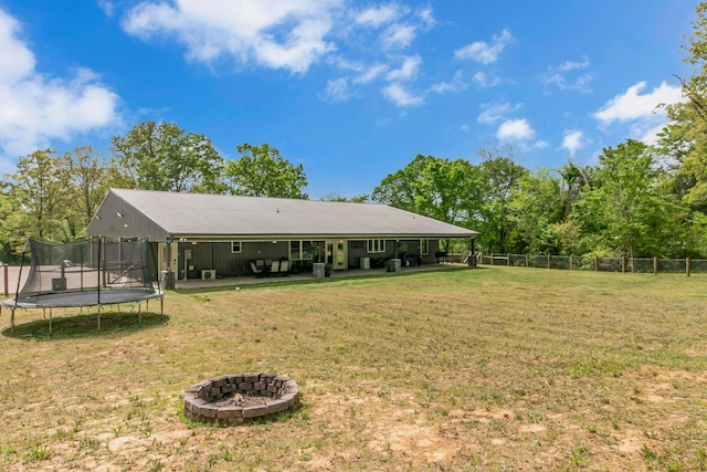 rear view of house featuring a yard, a trampoline, a fire pit, and fence