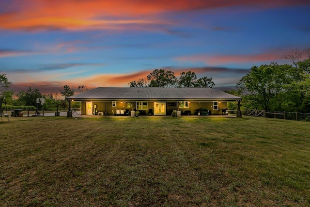 back of property at dusk with metal roof, fence, a yard, and a patio area