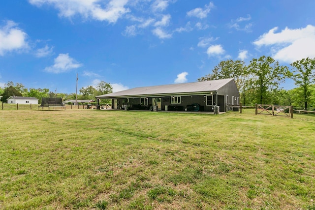 rear view of property featuring a lawn, a trampoline, a gate, and fence