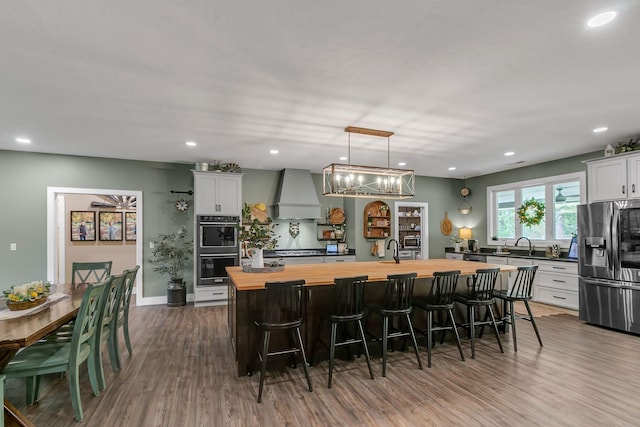 kitchen featuring wood counters, custom range hood, dark wood-type flooring, double wall oven, and stainless steel fridge with ice dispenser