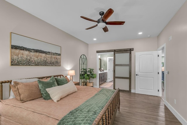bedroom featuring connected bathroom, a barn door, baseboards, recessed lighting, and wood finished floors
