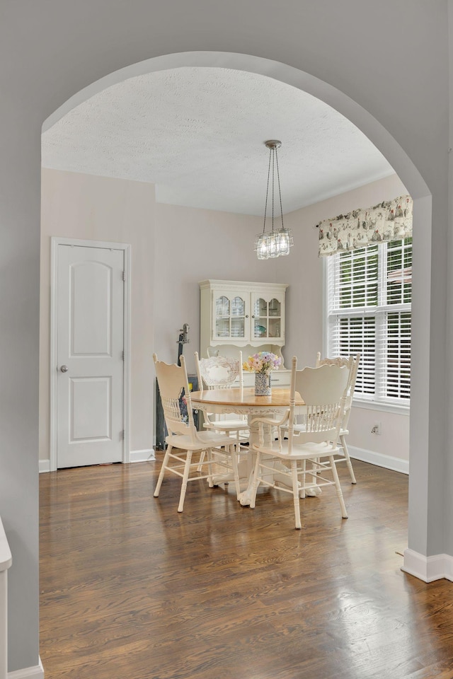 dining area featuring baseboards, wood finished floors, a textured ceiling, and arched walkways