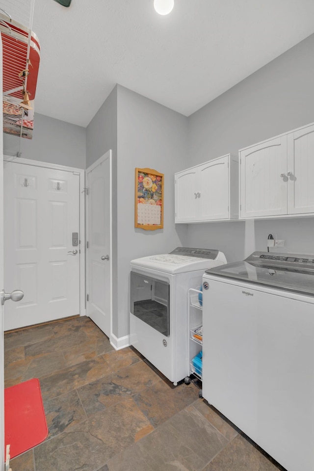 laundry room with washing machine and dryer, cabinet space, stone finish floor, and baseboards