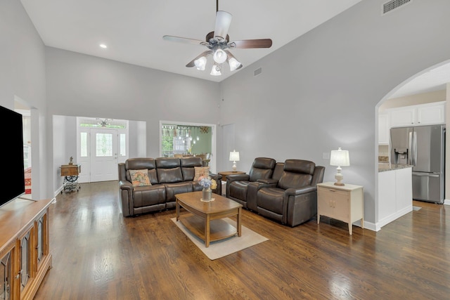 living room featuring visible vents, ceiling fan, arched walkways, dark wood-style flooring, and a high ceiling