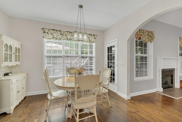 dining space featuring dark wood finished floors, arched walkways, a fireplace, baseboards, and a textured ceiling