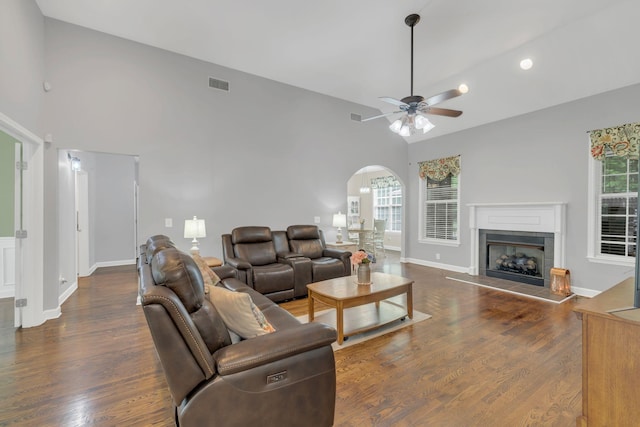 living room featuring a tile fireplace, arched walkways, a ceiling fan, and wood finished floors