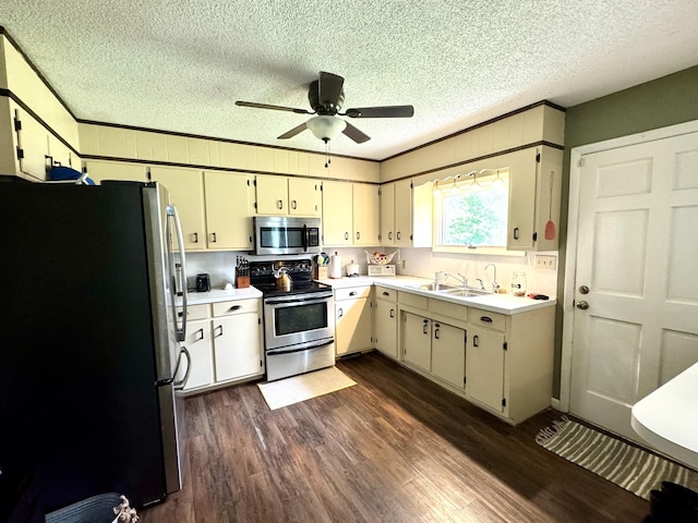 kitchen with a textured ceiling, a sink, stainless steel appliances, light countertops, and dark wood-style floors