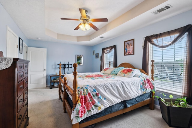 bedroom with light carpet, ceiling fan, baseboards, visible vents, and a tray ceiling