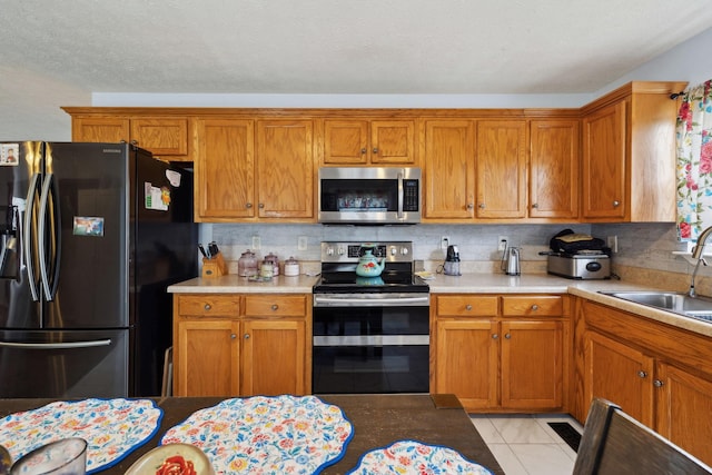 kitchen featuring stainless steel appliances, light countertops, brown cabinetry, and a sink