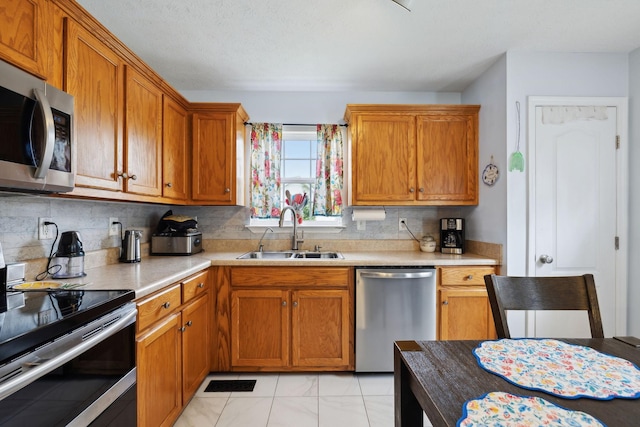 kitchen featuring tasteful backsplash, appliances with stainless steel finishes, light countertops, brown cabinets, and a sink