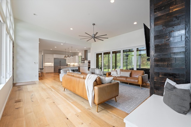 living area featuring light wood-style floors, ceiling fan, recessed lighting, and a high ceiling