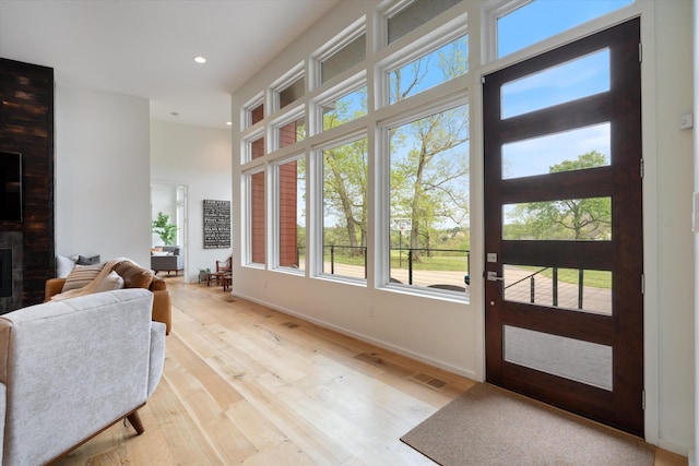 doorway to outside featuring light wood-style floors, baseboards, recessed lighting, a fireplace, and a towering ceiling