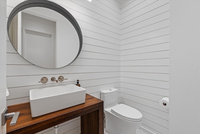 half bathroom featuring wooden walls, toilet, and vanity