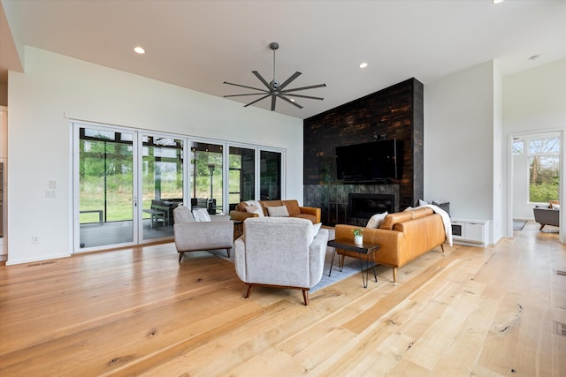 living area with light wood finished floors, a ceiling fan, high vaulted ceiling, and a tiled fireplace