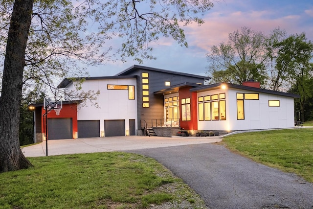 contemporary house featuring a chimney, aphalt driveway, an attached garage, and a lawn