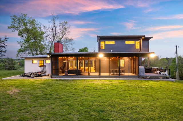 back of property at dusk with a lawn, a wooden deck, and a chimney