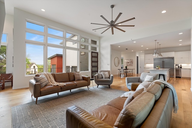 living room featuring recessed lighting, baseboards, light wood-type flooring, a ceiling fan, and a towering ceiling