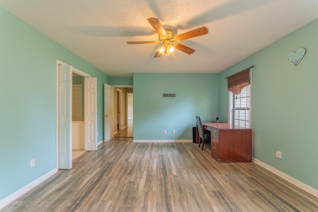 unfurnished office with a textured ceiling, ceiling fan, wood finished floors, and baseboards