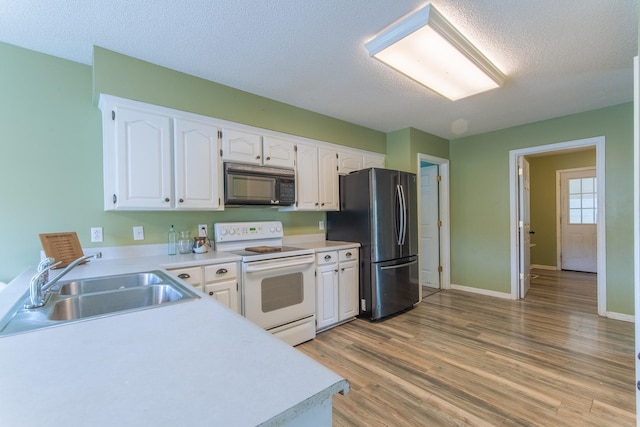 kitchen with a sink, black microwave, white cabinets, freestanding refrigerator, and electric range