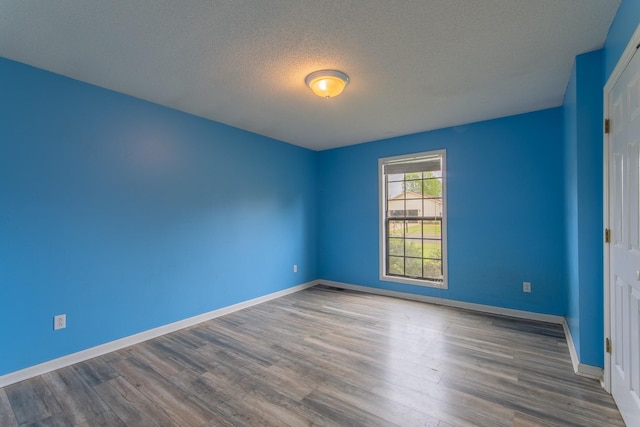 spare room with a textured ceiling, wood finished floors, and baseboards