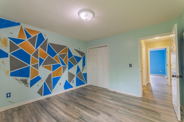 empty room with a textured ceiling, an accent wall, wood finished floors, and baseboards