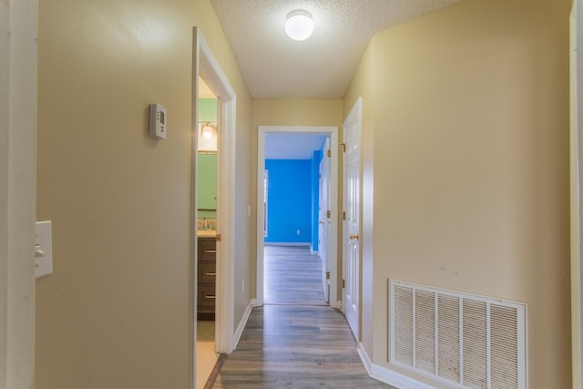 hallway with a textured ceiling, visible vents, wood finished floors, and baseboards