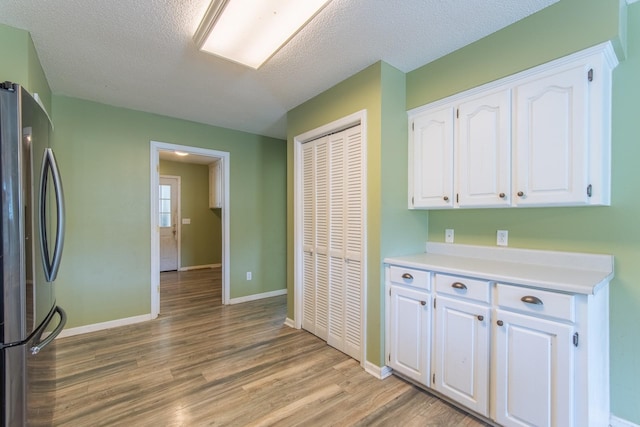 kitchen featuring light wood-style floors, light countertops, baseboards, white cabinets, and freestanding refrigerator
