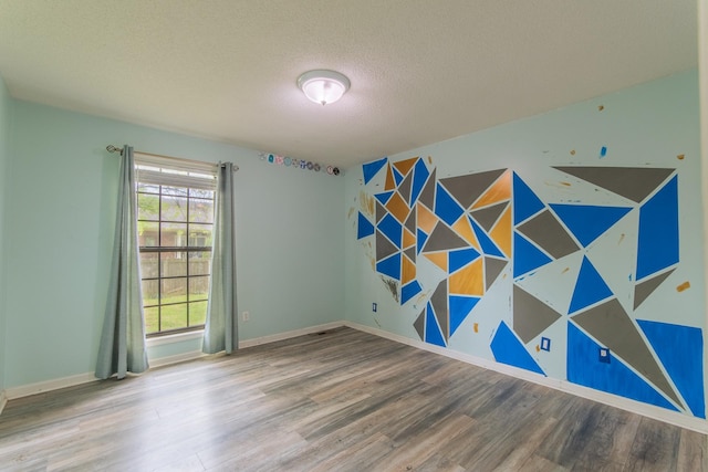 empty room featuring baseboards, an accent wall, wood finished floors, and a textured ceiling