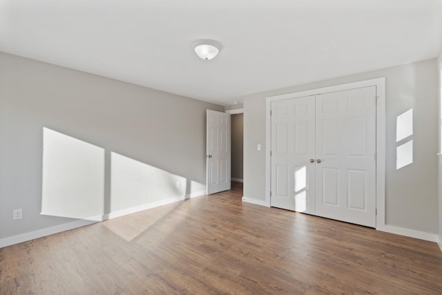 unfurnished bedroom with baseboards, wood finished floors, and a closet