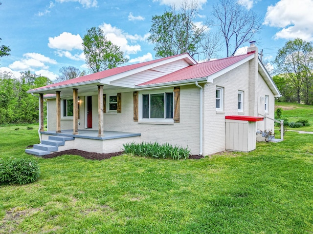ranch-style house with a porch, a front yard, brick siding, metal roof, and a chimney