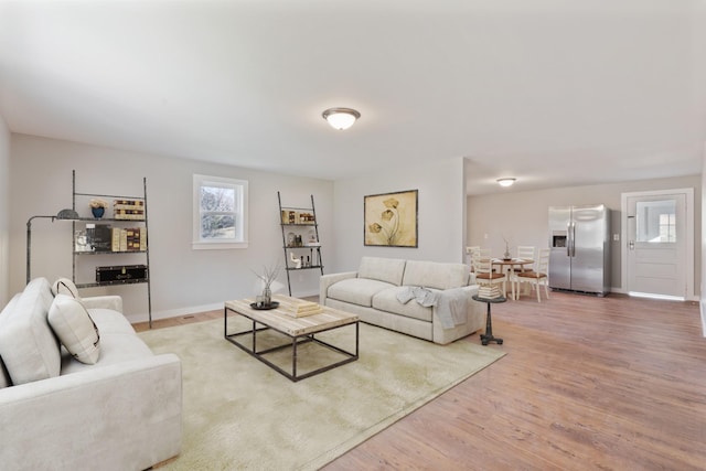 living room featuring baseboards, a healthy amount of sunlight, and light wood finished floors