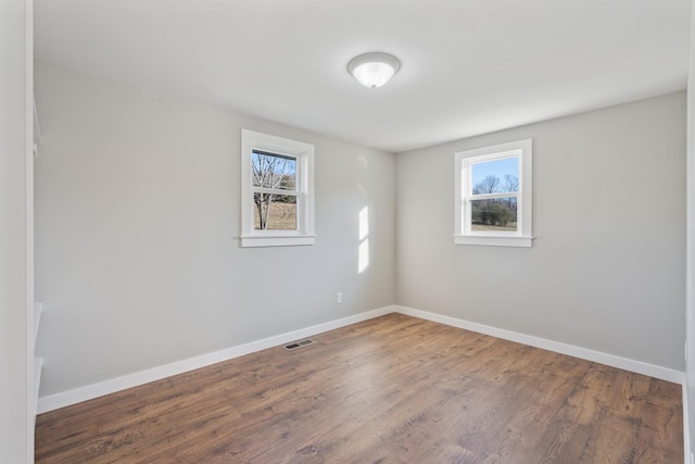 spare room with wood finished floors, visible vents, and baseboards