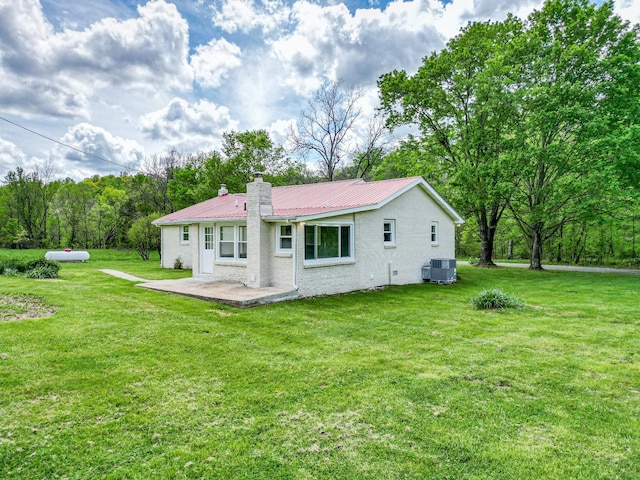 rear view of house featuring a chimney, metal roof, a patio area, central air condition unit, and a yard